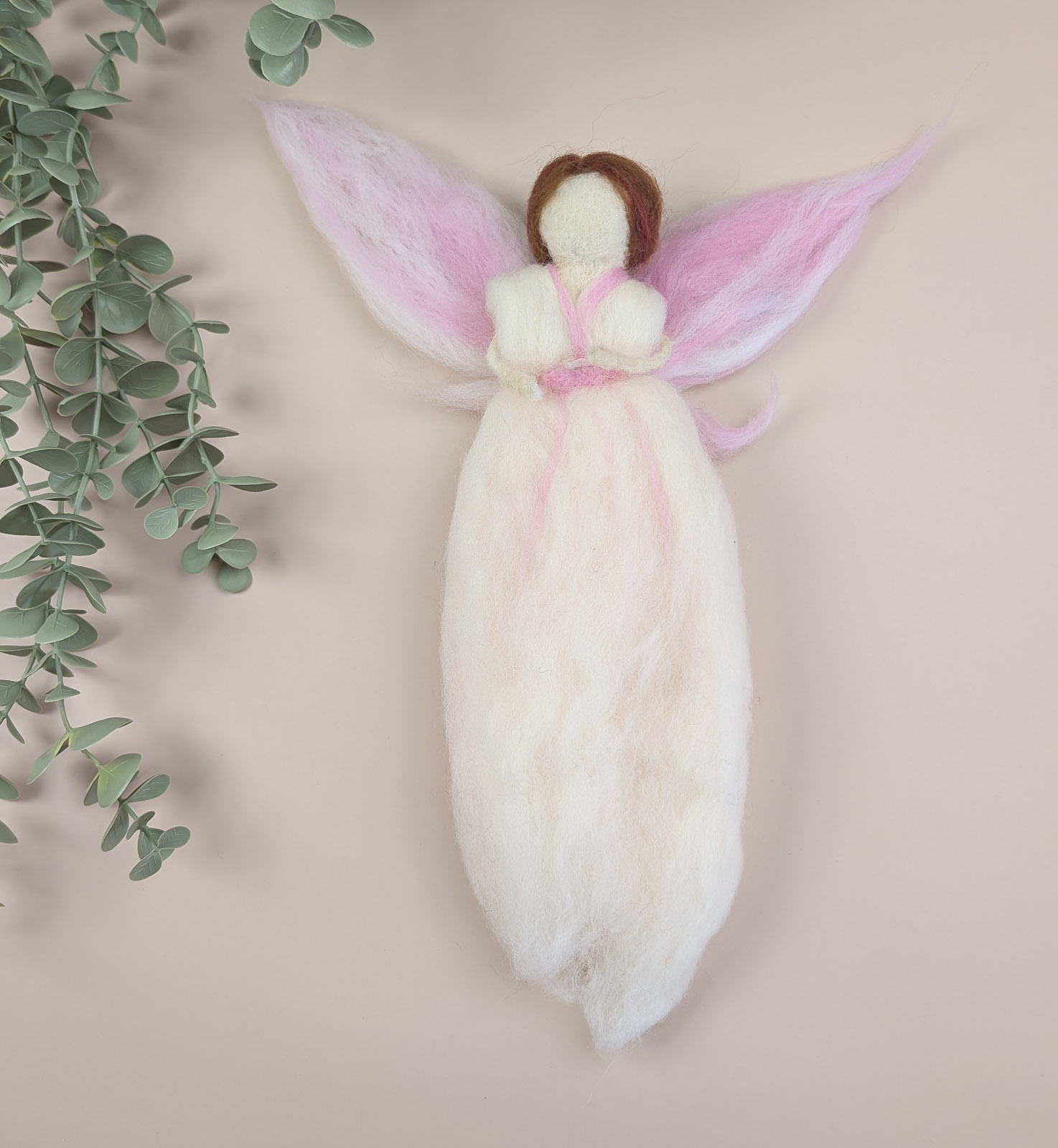 nåltovad ängel i vit ull med brunt hår och rosa vingar